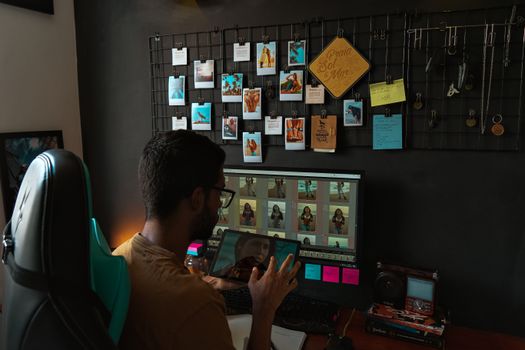 Young man editing photos on a computer at a stylish office desk with a display grid above.