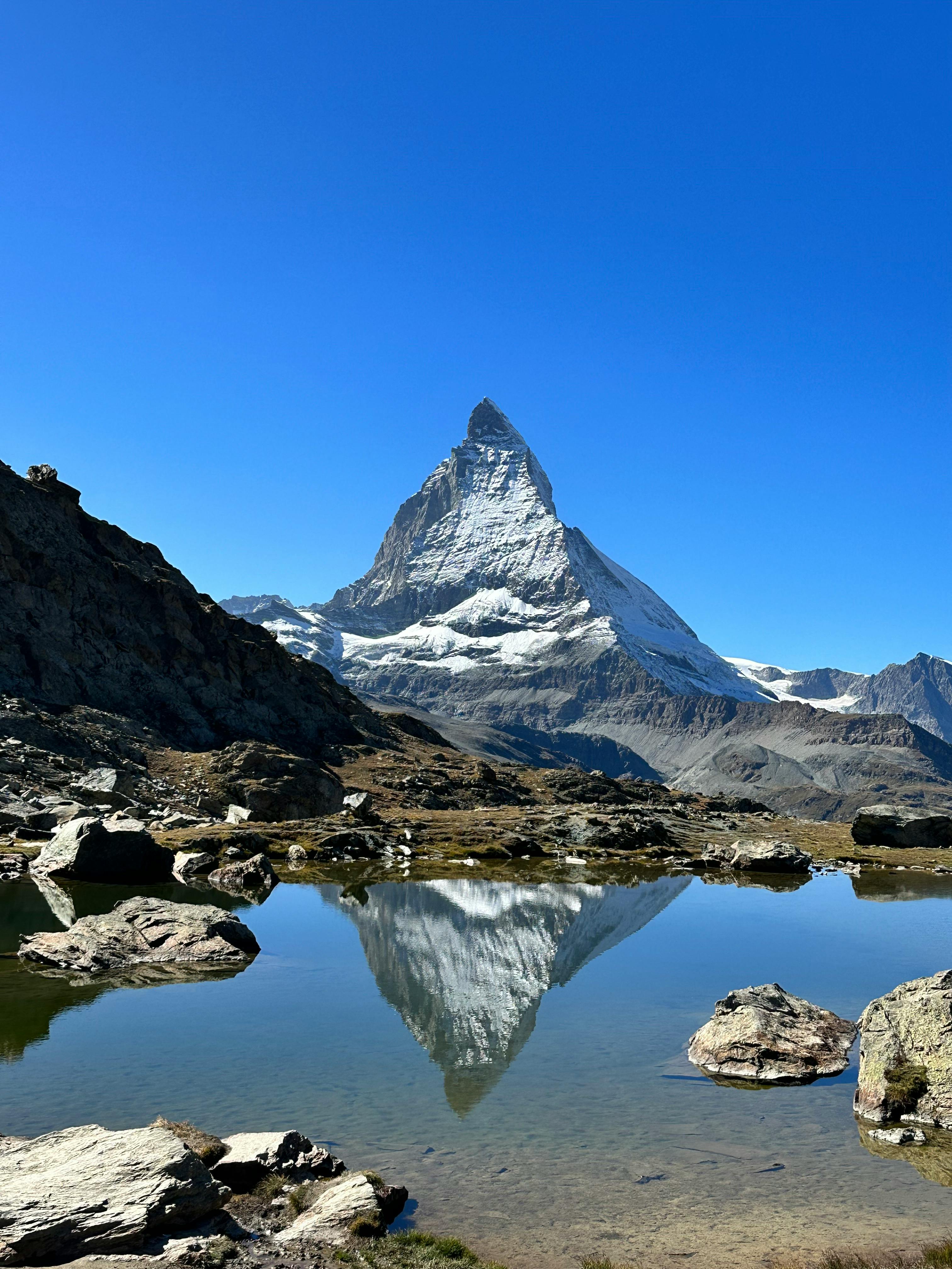 Beautiful reflection of Matterhorn in a serene alpine lake under a clear blue sky in Zermatt, Switzerland.