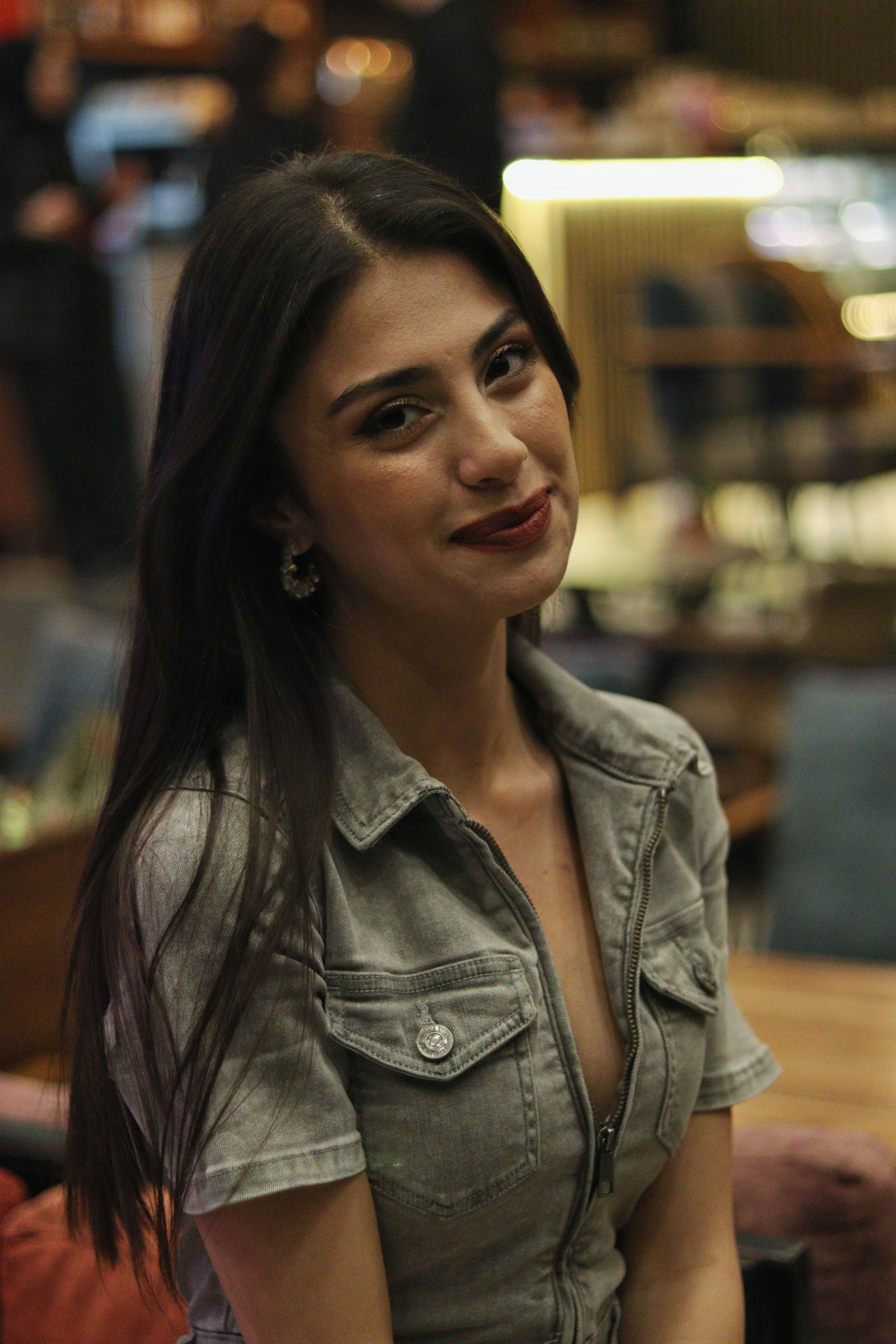 A woman in a gray blouse smiling while sitting in a cozy restaurant.