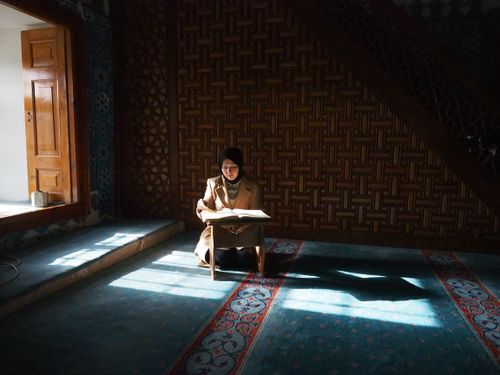 Free A Muslim woman wearing a hijab reads the Quran in the sunlit prayer room of a mosque. Stock Photo