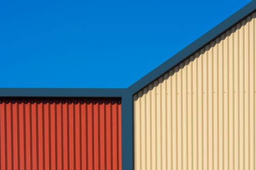 Free A modern building facade with red and beige corrugated iron against a clear blue sky. Stock Photo