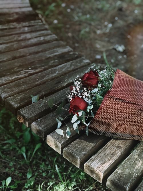 Free A beautiful bouquet of red roses resting on a rustic wooden bench in an outdoor setting in Türkiye. Stock Photo