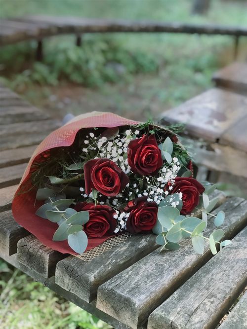 Free A stylish bouquet of red roses with baby's breath on a rustic wooden bench outdoors. Stock Photo