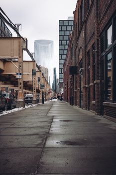 A city street lined with brick buildings and modern skyscrapers on a cloudy day.