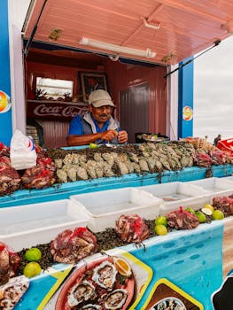 Seafood vendor selling fresh oysters and fish at a lively food stall, colorful display.