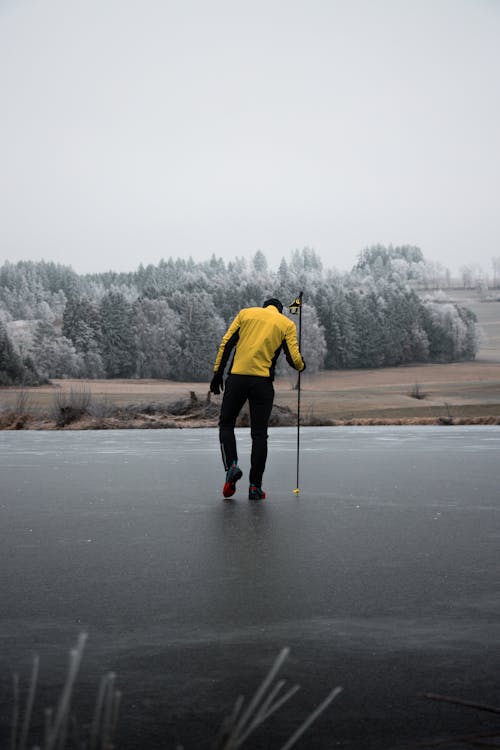 Person in Yellow Jacket Standing on Frozen Lake