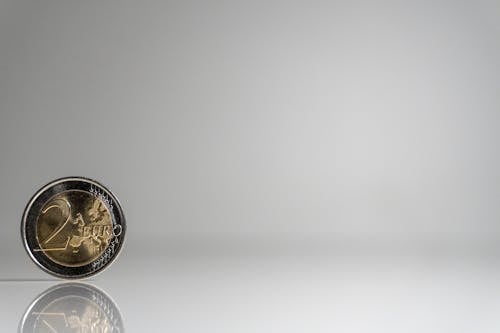Free A single 2 Euro coin standing on a reflective surface against a plain background. Stock Photo