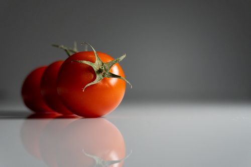 Free Minimalist image of three vibrant cherry tomatoes reflecting on a shiny surface. Stock Photo