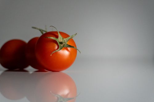 Free Vivid and detailed image of cherry tomatoes on a reflective surface, perfect for food photography. Stock Photo