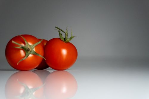 Free Three vibrant cherry tomatoes with green stems, perfectly lit in a studio setting. Stock Photo