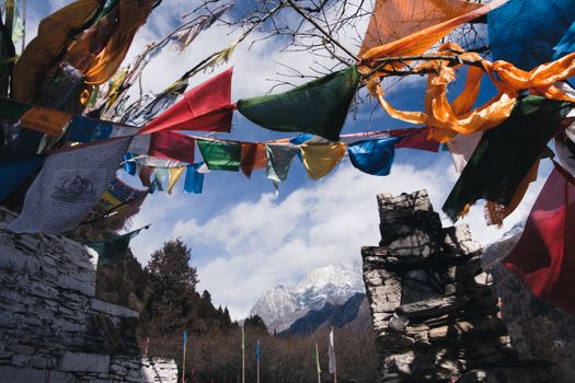 Vivid prayer flags flutter against a mountain backdrop under a blue sky.