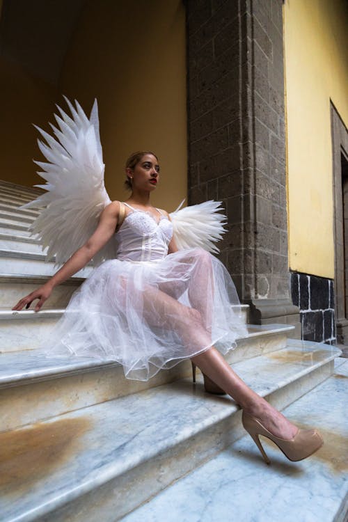 Woman in White Dress with Angel Wings Sitting on Stairs