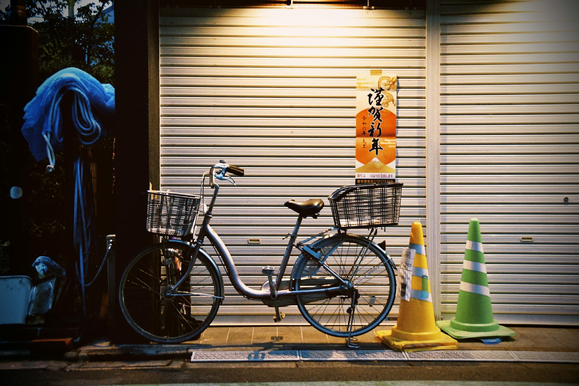 A bicycle with baskets parked beside green and yellow traffic cones in an urban Japanese street at night.