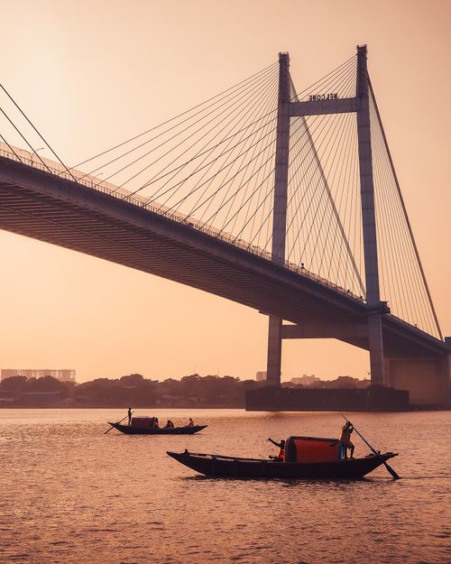 Free Boats glide beneath Vidyasagar Setu in Kolkata at sunset, capturing a serene cityscape. Stock Photo