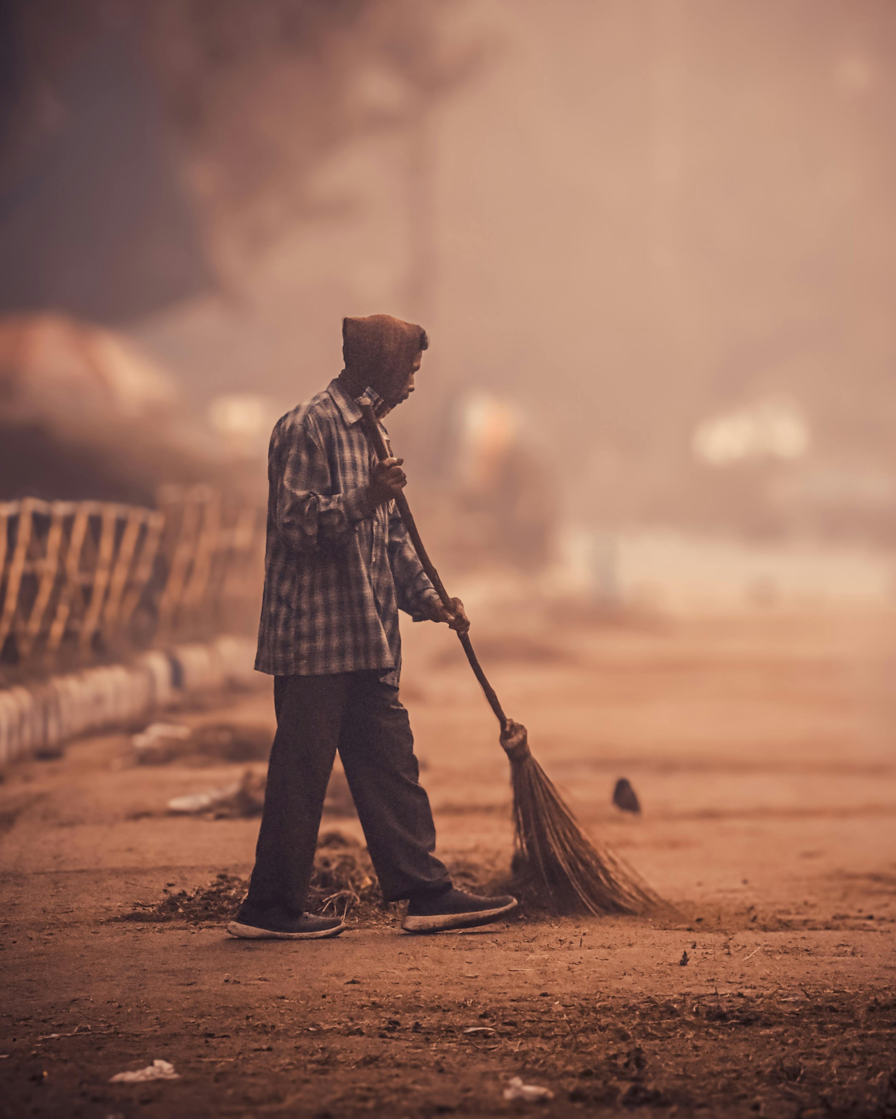A dedicated street cleaner sweeps a deserted urban sidewalk at dawn, creating a serene atmosphere.