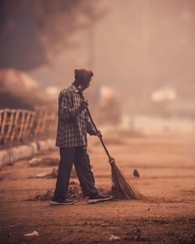 A dedicated street cleaner sweeps a deserted urban sidewalk at dawn, creating a serene atmosphere.