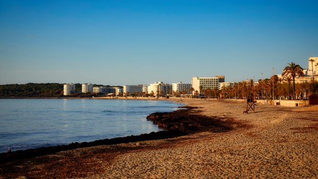 Beautiful sunset over Cala Millor beach with seaside hotels and palm trees.