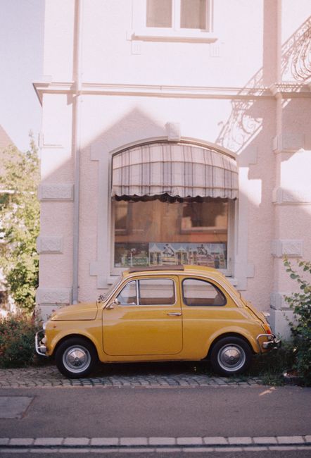 Charming vintage yellow Fiat 500 parked against a pastel building in Switzerland.