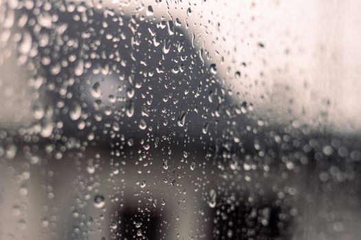 Close-up of raindrops on a window pane with a blurred outdoor scene.