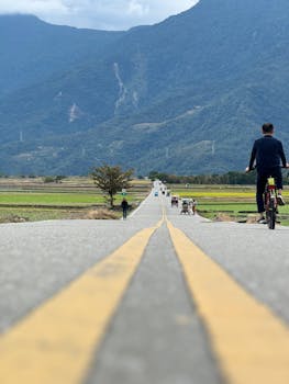 Cyclist riding along a scenic rural road in Taiwan's lush countryside with mountains in the background.