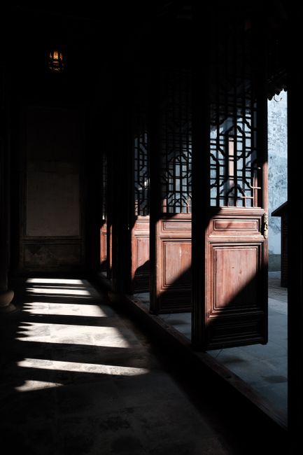 Explore the beauty of sunlight casting intricate shadows on an ancient wooden doorway within an old temple.