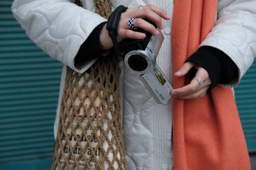 Detailed view of hands holding a vintage handycam with colorful outfit and netted bag.