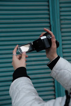 A person in a white jacket holding a camcorder with an LCD display outdoors.