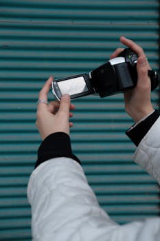 Close-up of hands holding a retro camcorder with a teal striped background. Perfect for vintage technology themes.