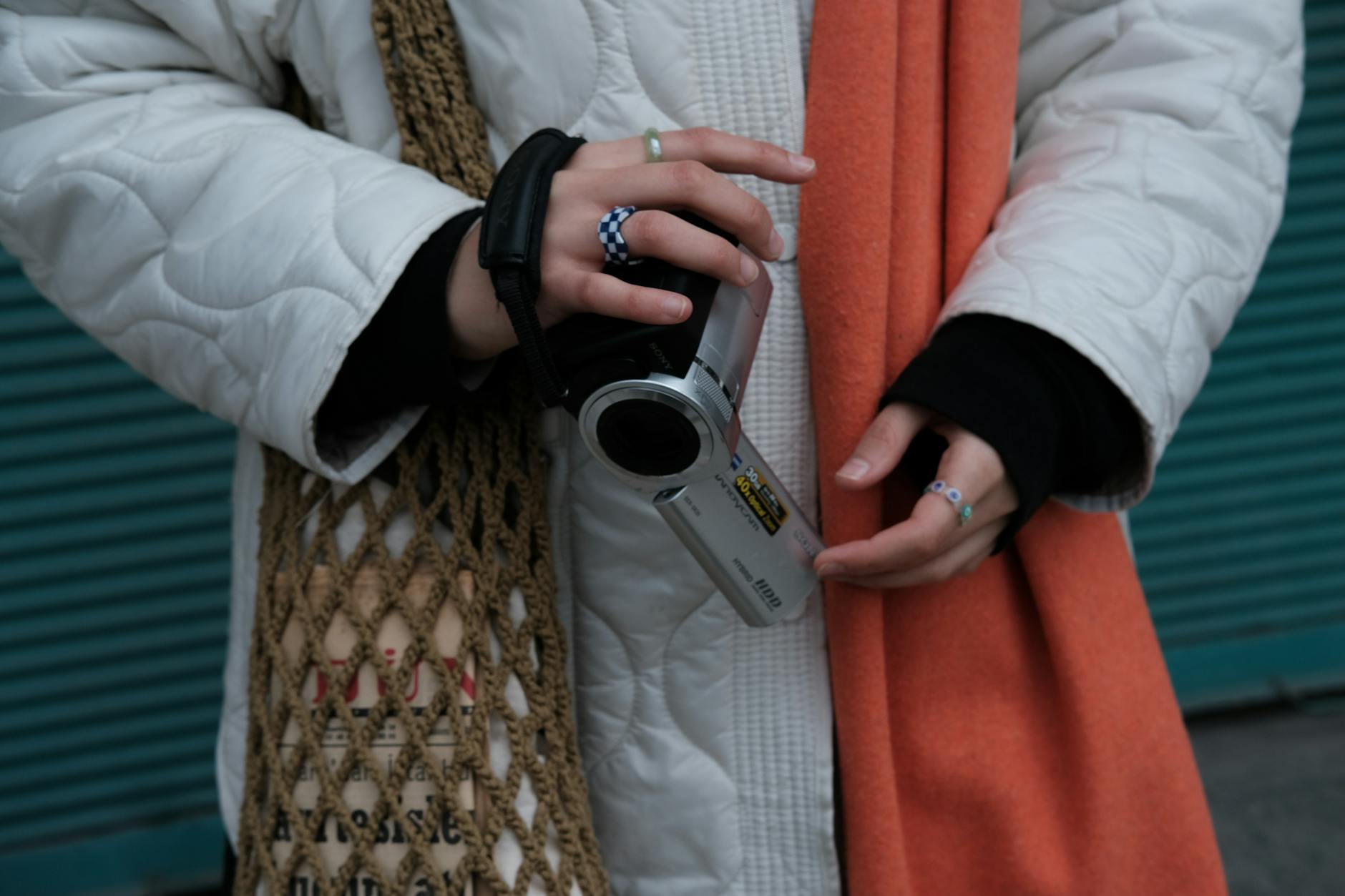 Hands holding a vintage camcorder with stylish accessories, blending technology and fashion.