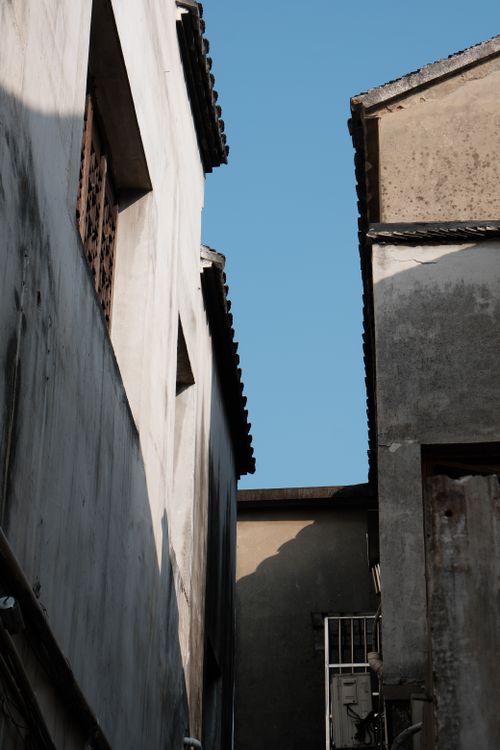Free A narrow alleyway framed by rustic gray walls under a clear blue sky, showcasing urban charm. Stock Photo