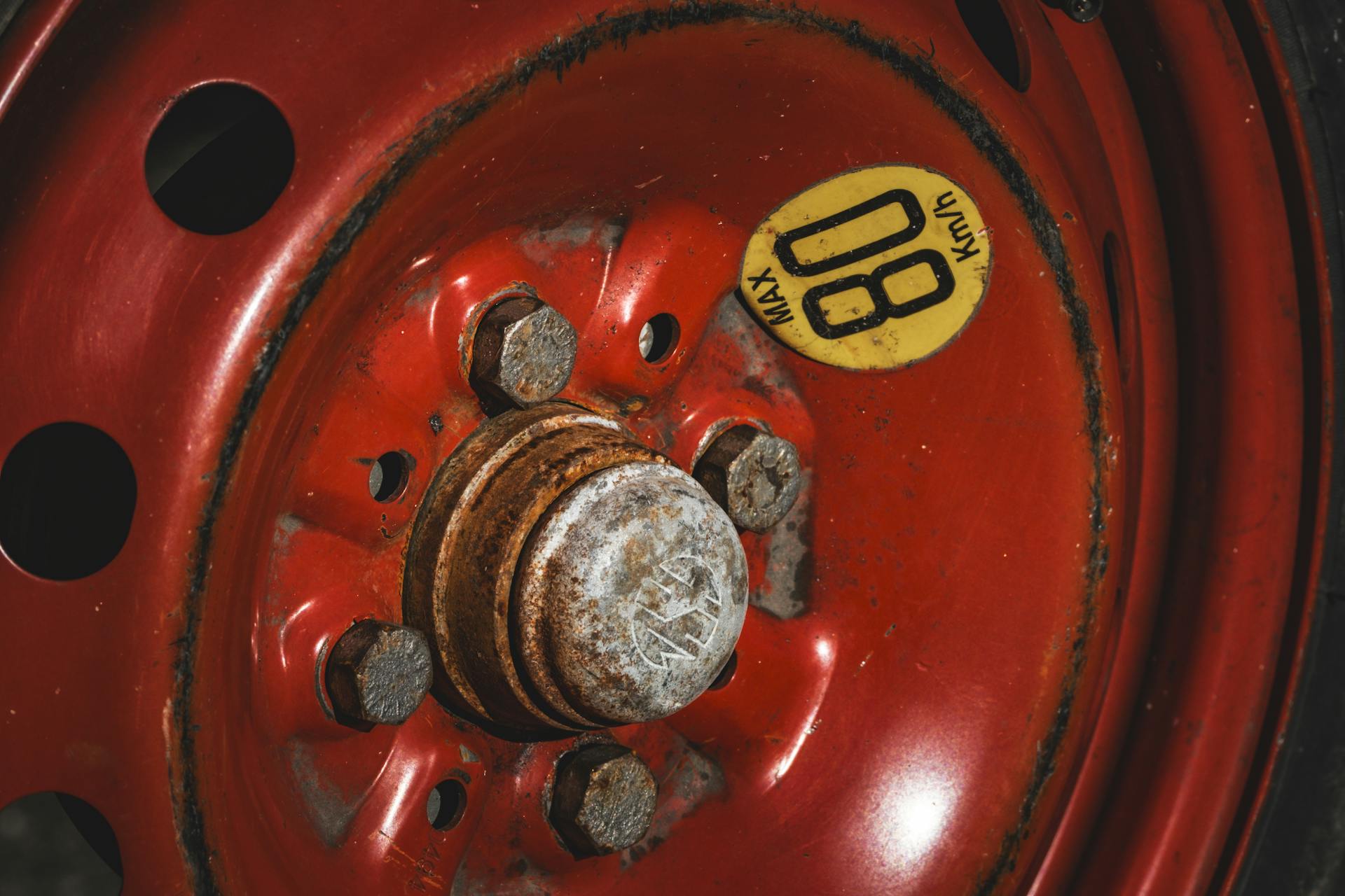 Detailed view of a rusty red spare car wheel with an '80 KM/H' max speed warning label.