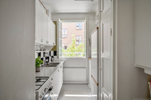 A bright and contemporary small kitchen with white cabinets and open window.