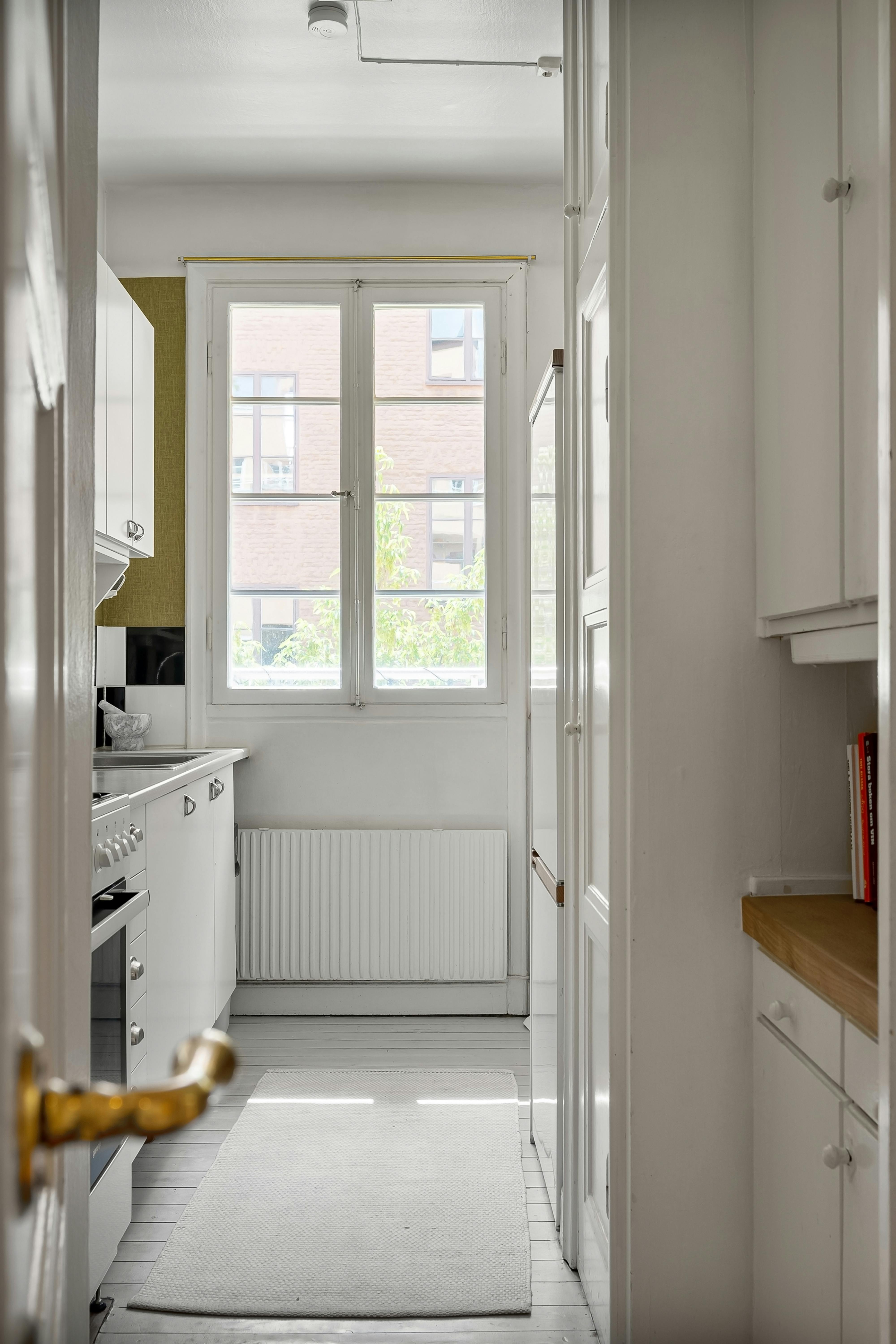 A modern white kitchen featuring large windows and sleek appliances.