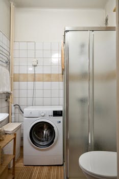A compact bathroom featuring a shower, washing machine, and toilet for efficient space use.