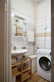 Compact bathroom with a washing machine, washbasin, and wooden shelving for a modern interior design look.