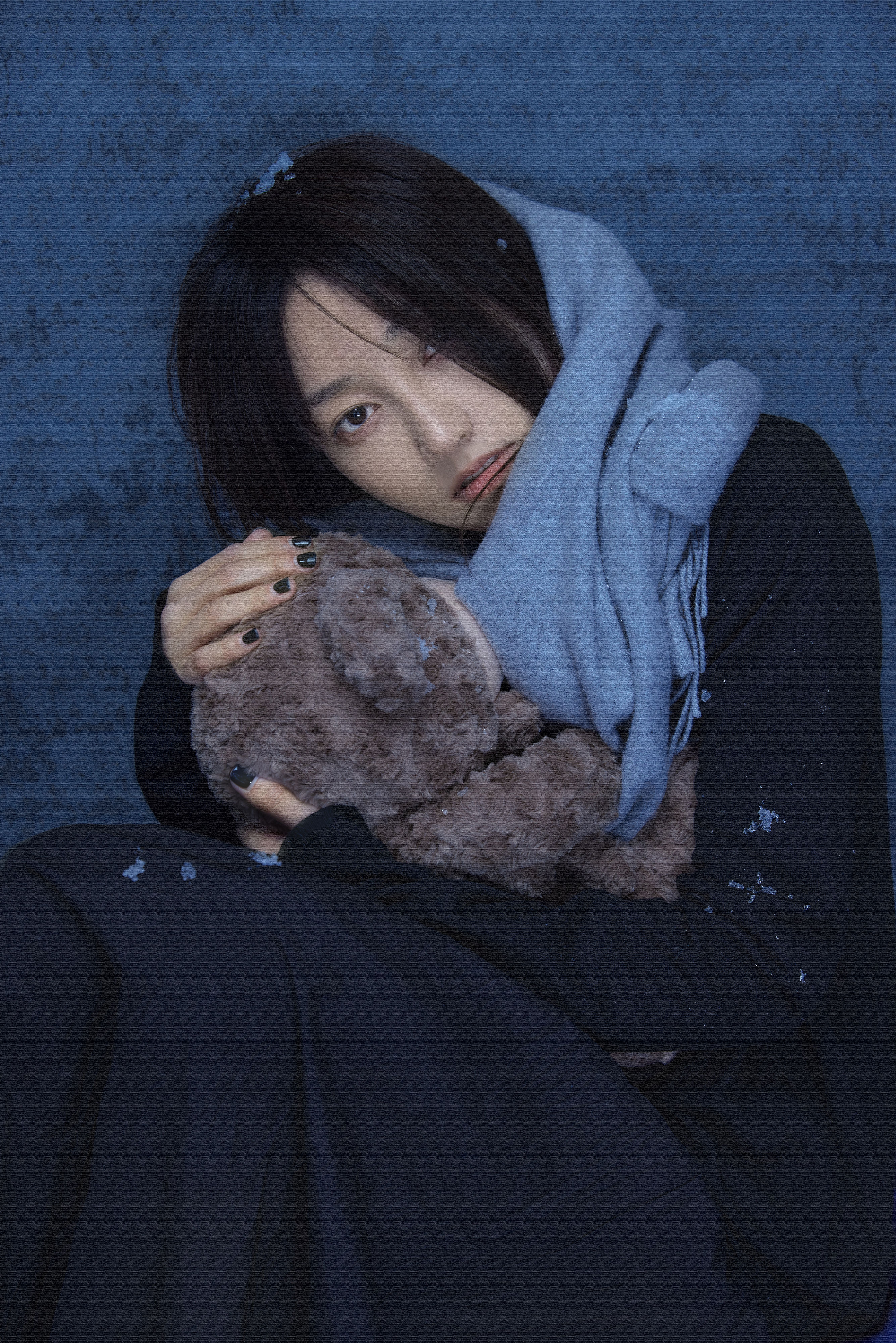 A woman in winter clothing embracing a teddy bear, conveying a mood of uncertainty and warmth.