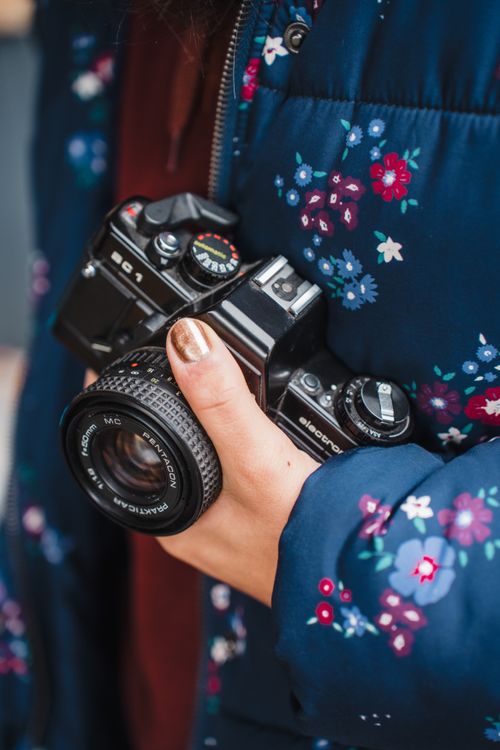Free A woman in a floral jacket holds a classic film camera, showcasing a passion for photography. Stock Photo