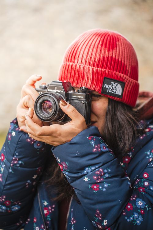 Free A woman in a red beanie capturing a photo with a vintage camera outdoors. Stock Photo