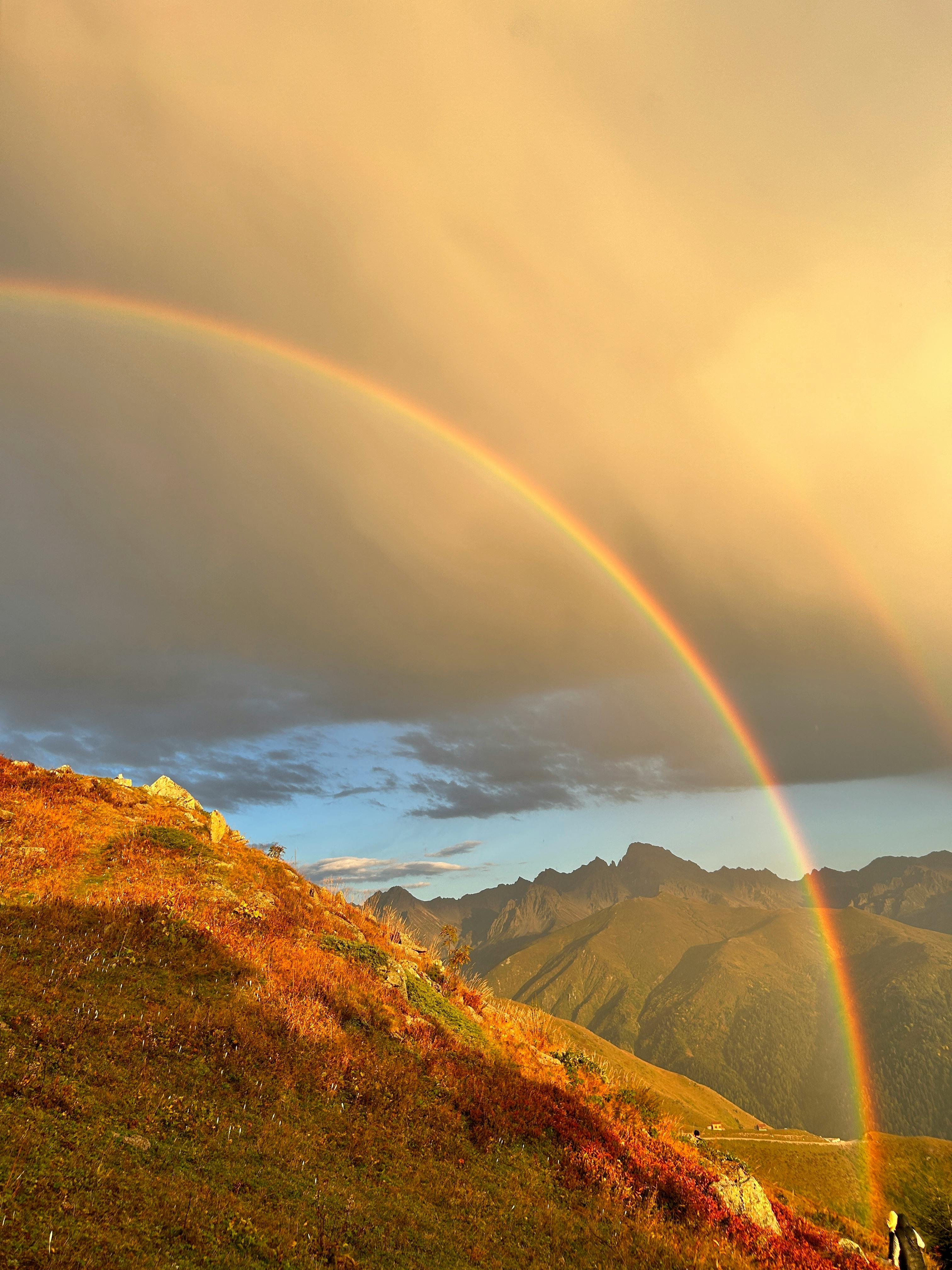A stunning rainbow arches over a mountainous landscape during sunset in Rize, Türkiye. Captivating natural beauty.