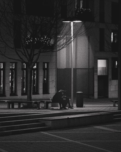 Free A solitary person sits on a bench under a streetlight in this dramatic urban night scene. Stock Photo