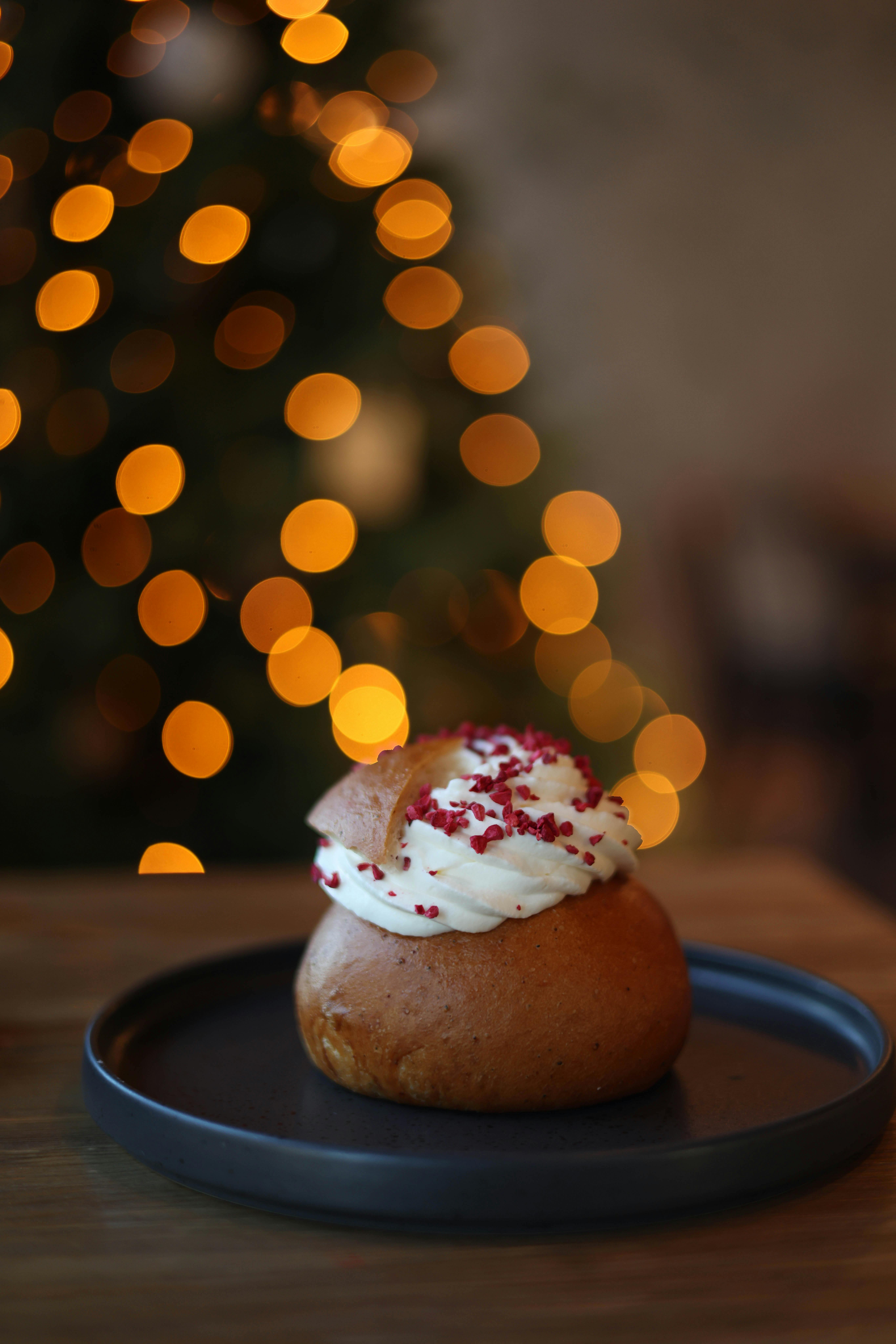 Delicious Swedish semla pastry on plate with festive bokeh lights in the background.