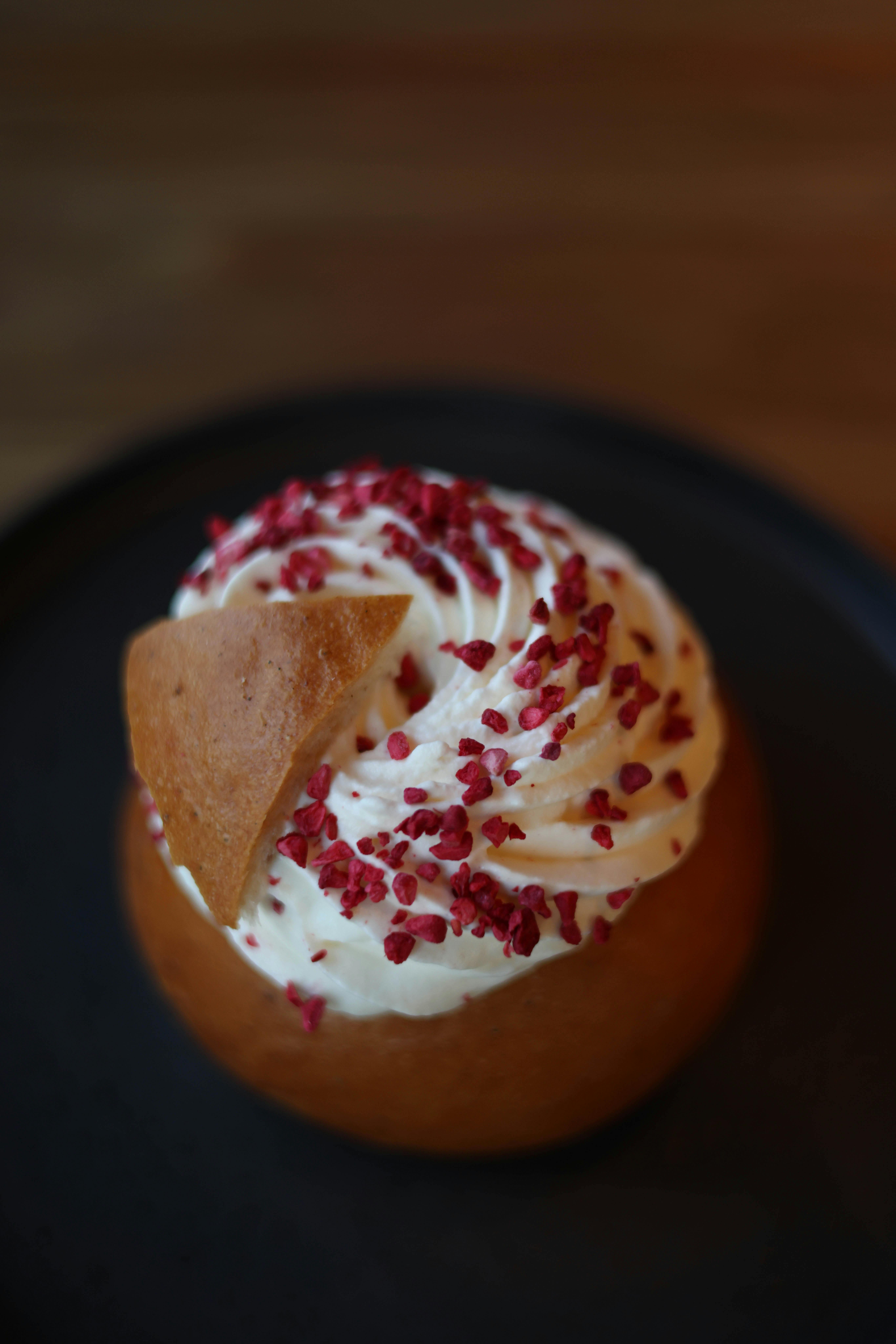 Top view of a Swedish semla bun garnished with cardamom and whipped cream, served on a dark plate.