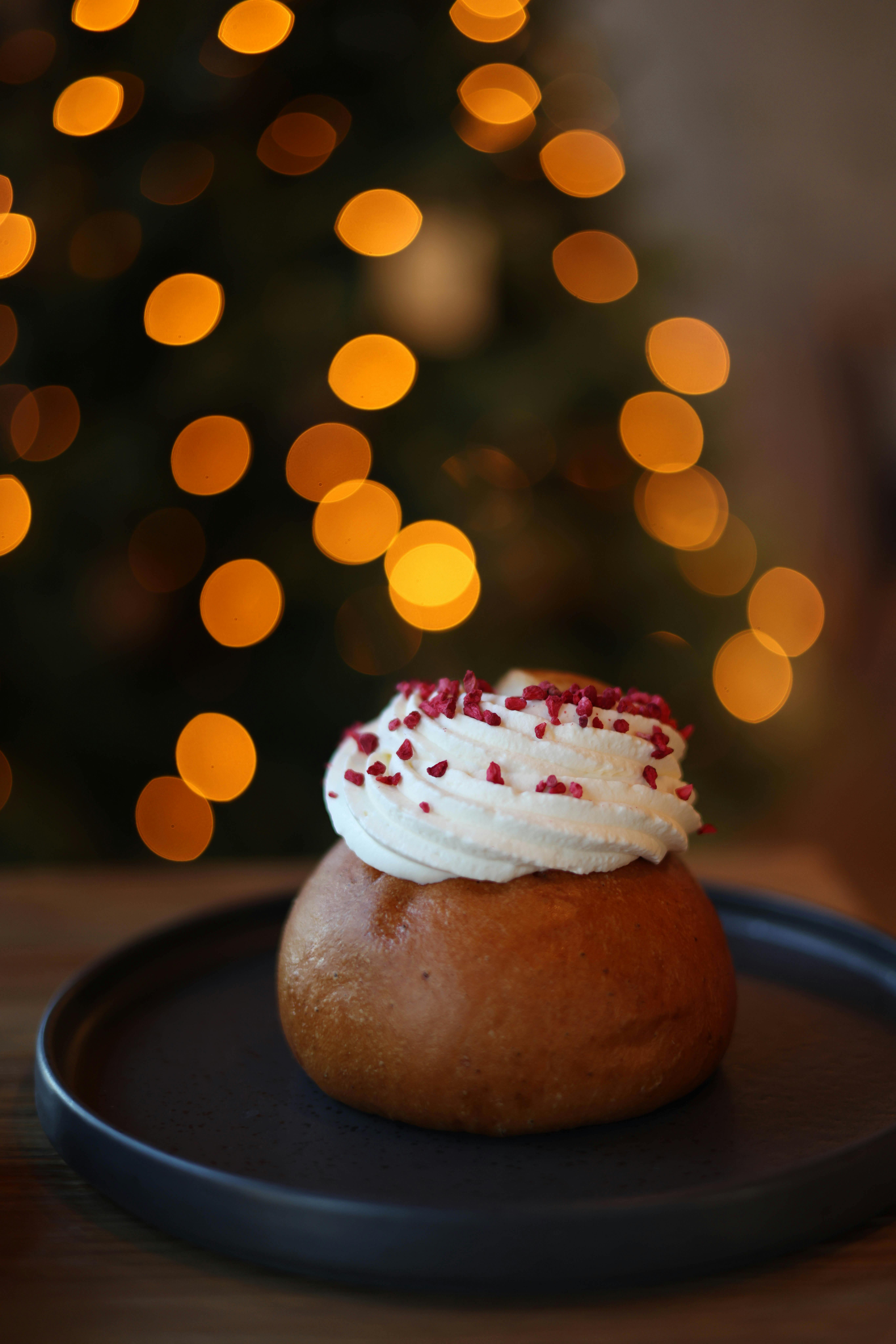 A traditional Swedish semla bun topped with whipped cream on a plate, festive bokeh in the background.