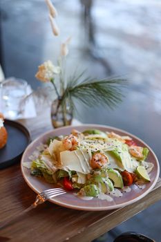 Plate of Caesar salad with shrimp, avocado, and Parmesan cheese garnished elegantly.
