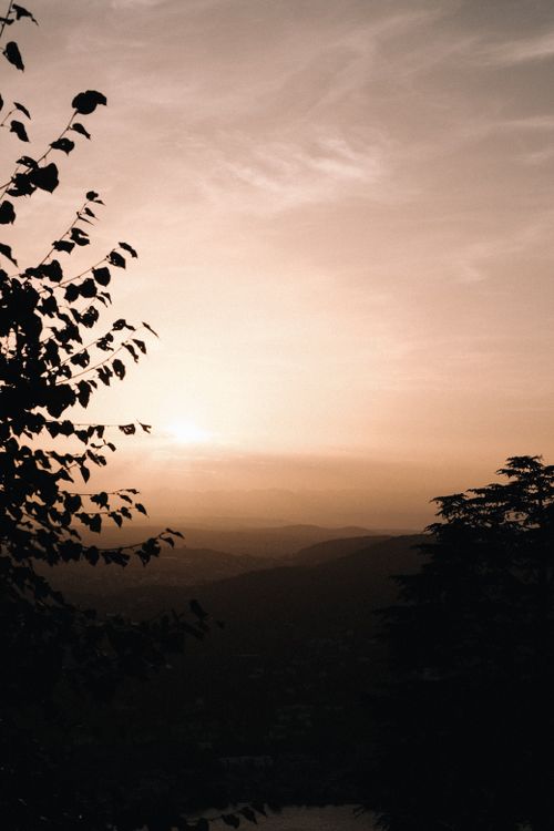 Free Peaceful sunrise with sun peeking over hills, framed by silhouettes of trees. Stock Photo