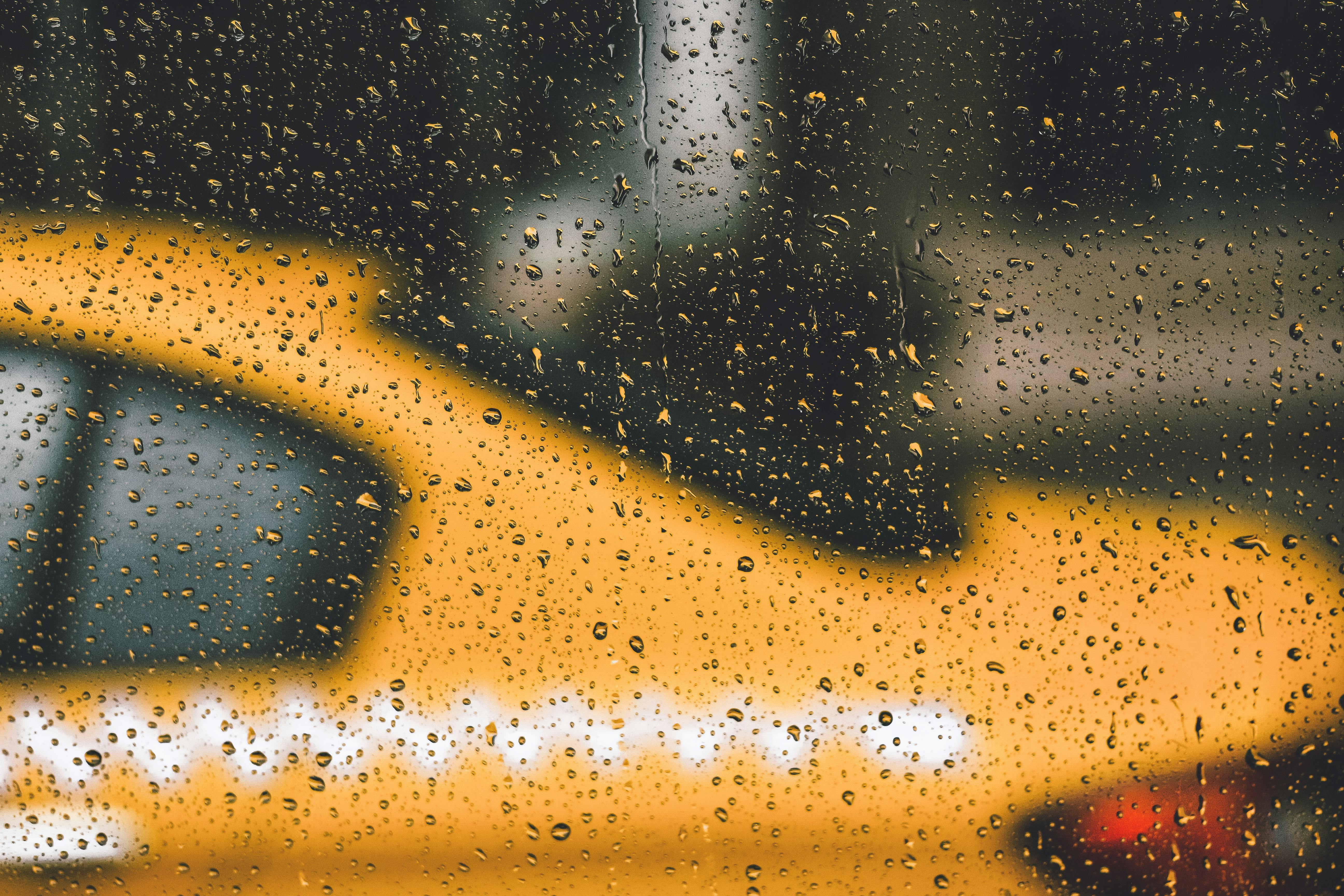 Blurry yellow taxi seen through rain-covered window in city, creating a moody urban vibe.