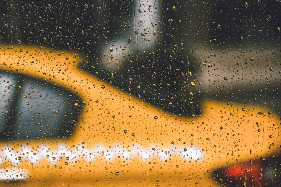 Blurry yellow taxi seen through rain-covered window in city, creating a moody urban vibe.