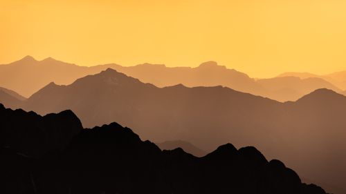 Free Silhouetted mountain ranges beneath a vibrant amber sky, capturing a tranquil sunset. Stock Photo