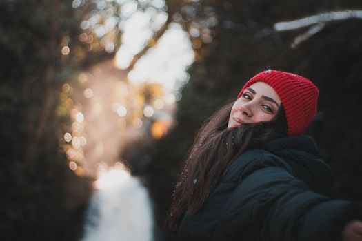 Smiling young woman in a red hat enjoying a winter day outside surrounded by trees and snow.