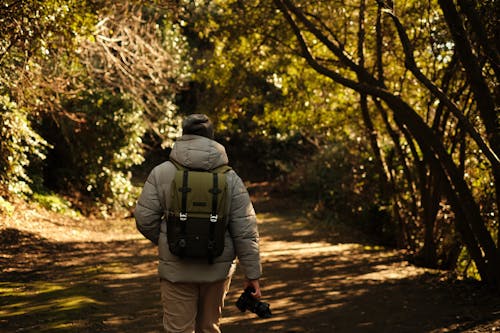 Back View of a Man with a Backpack and a Camera Walking in a Park 